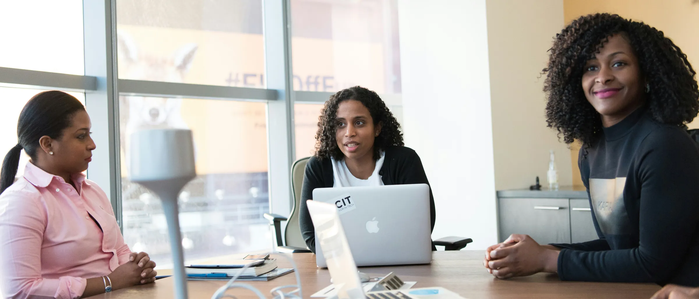 Three colleagues talking around a laptop in a bright meeting room